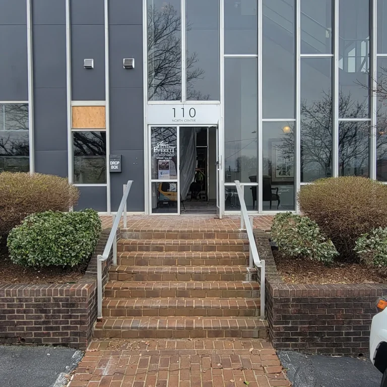 Exterior of a commercial office building at 110 North Center with tall, narrow tinted windows and a brick entryway with railings and trimmed bushes.