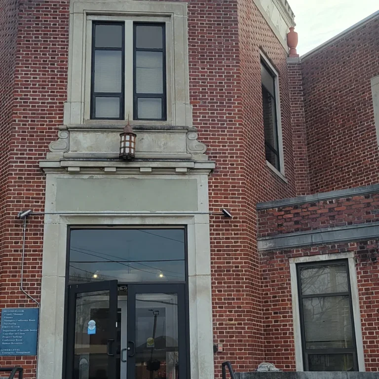 Historic red brick building with dark tinted windows and a modern glass entry door framed by stone accents, combining classic architecture with updated privacy features.