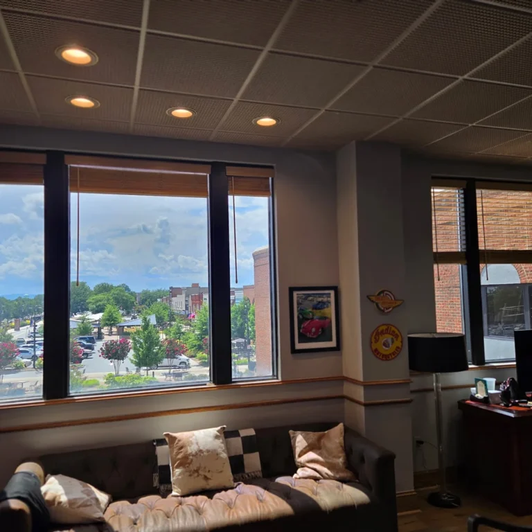 Interior of a cozy office with tinted floor-to-ceiling windows, offering a clear view of a city street and greenery while reducing glare on furniture and décor.