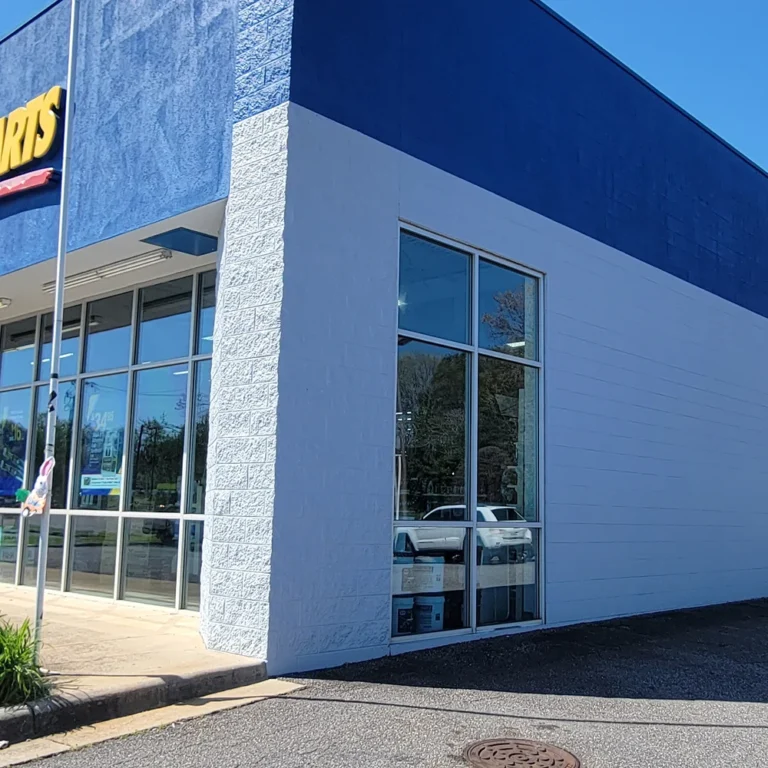 Exterior of a commercial auto parts store with large untinted glass windows and a bold blue and white facade under a clear sky.