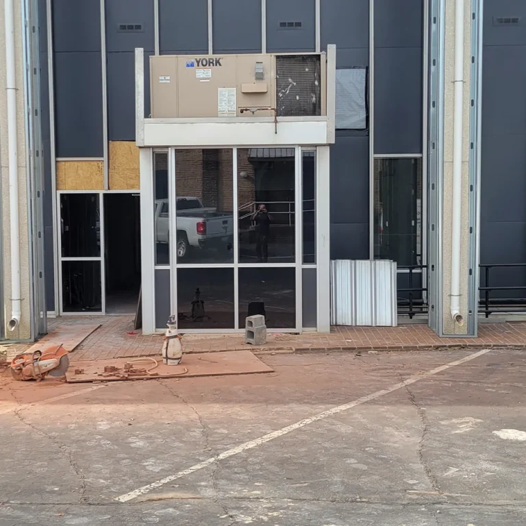 Commercial building under renovation with reflective tinted windows installed on the ground level and construction materials scattered across the entrance area.