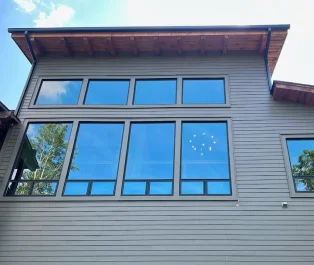 Large residential windows with a reflective tint installed on the upper floor of a modern home, showing reduced glare and clear reflections of trees and sky.