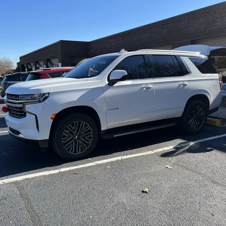 White Chevrolet Tahoe SUV with dark privacy window tint parked outside a commercial tinting shop on a sunny day.