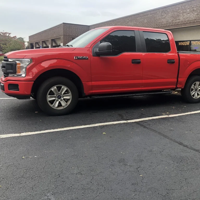 Red Ford F-150 pickup truck with freshly tinted windows parked outside a commercial window tinting shop.