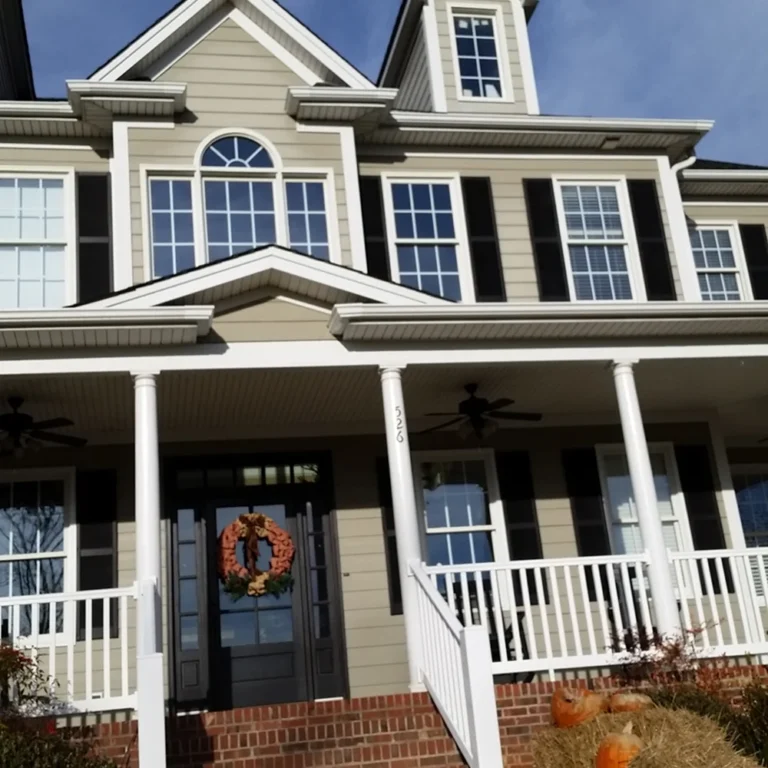 Two-story suburban home with large, grid-style tinted windows and a decorative fall wreath on the front door, featuring a beige exterior with white trim and black shutters.