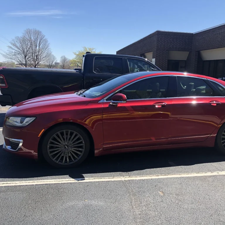 Shiny red sedan with tinted windows parked in front of a commercial building on a sunny day.