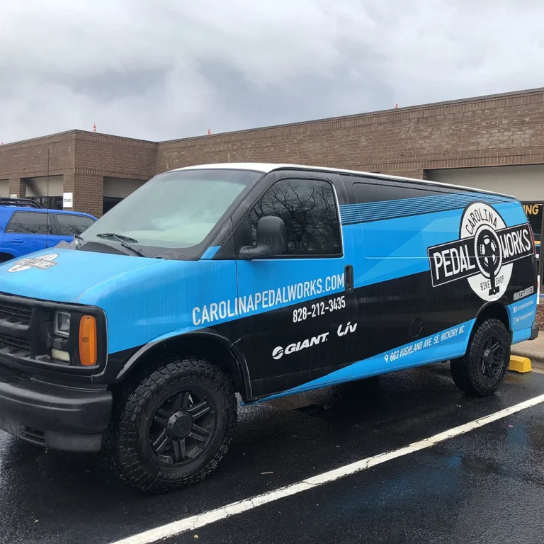 Carolina Pedal Works van with custom blue and black vinyl wrap parked outside a commercial building.