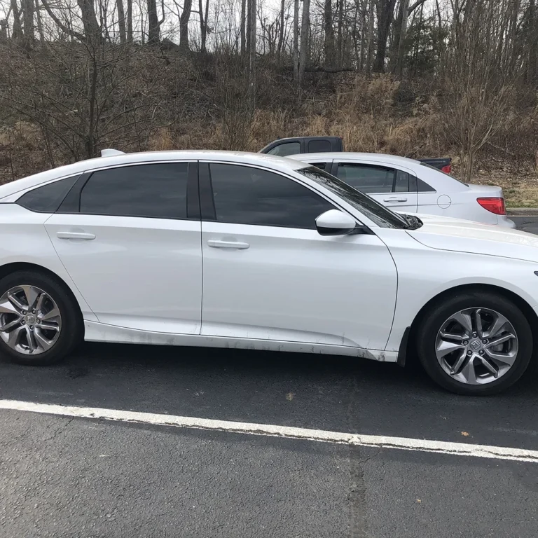 White sedan with dark tinted windows parked in a lot near a wooded area, providing a sleek appearance and added interior privacy.