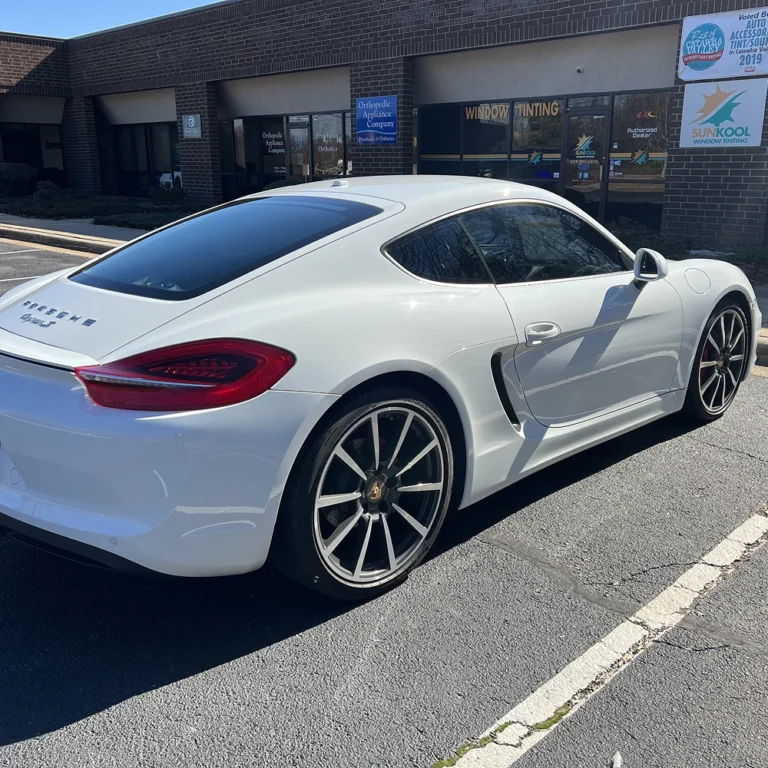 White Porsche Cayman S with tinted windows parked outside Sun Kool Window Tinting shop.