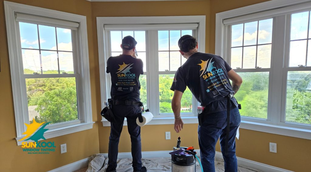 Two Sun-Kool Window Tinting professionals install window film on a sunny day inside a home with a view of lush greenery in Hickory, NC. This image illustrates the process of applying residential window tint to reduce glare and improve energy efficiency, helping answer the question: what is residential window tinting.