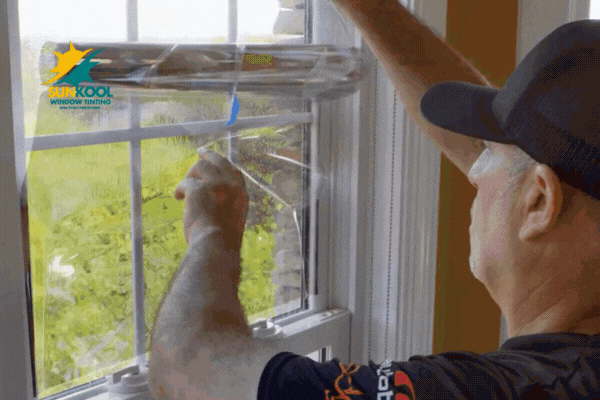 A Sun-Kool technician carefully applies residential window tinting film to a paneled window using a smoothing tool, highlighting the precision of professional installation in a sunlit home.