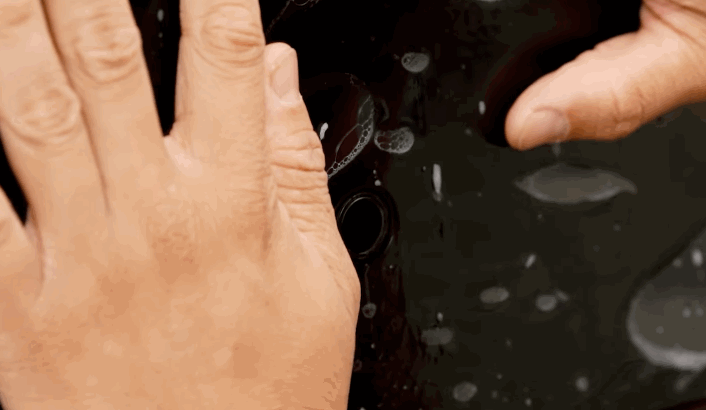 Hands smoothing paint protection film onto a glossy black car surface, ensuring full adhesion without air bubbles.