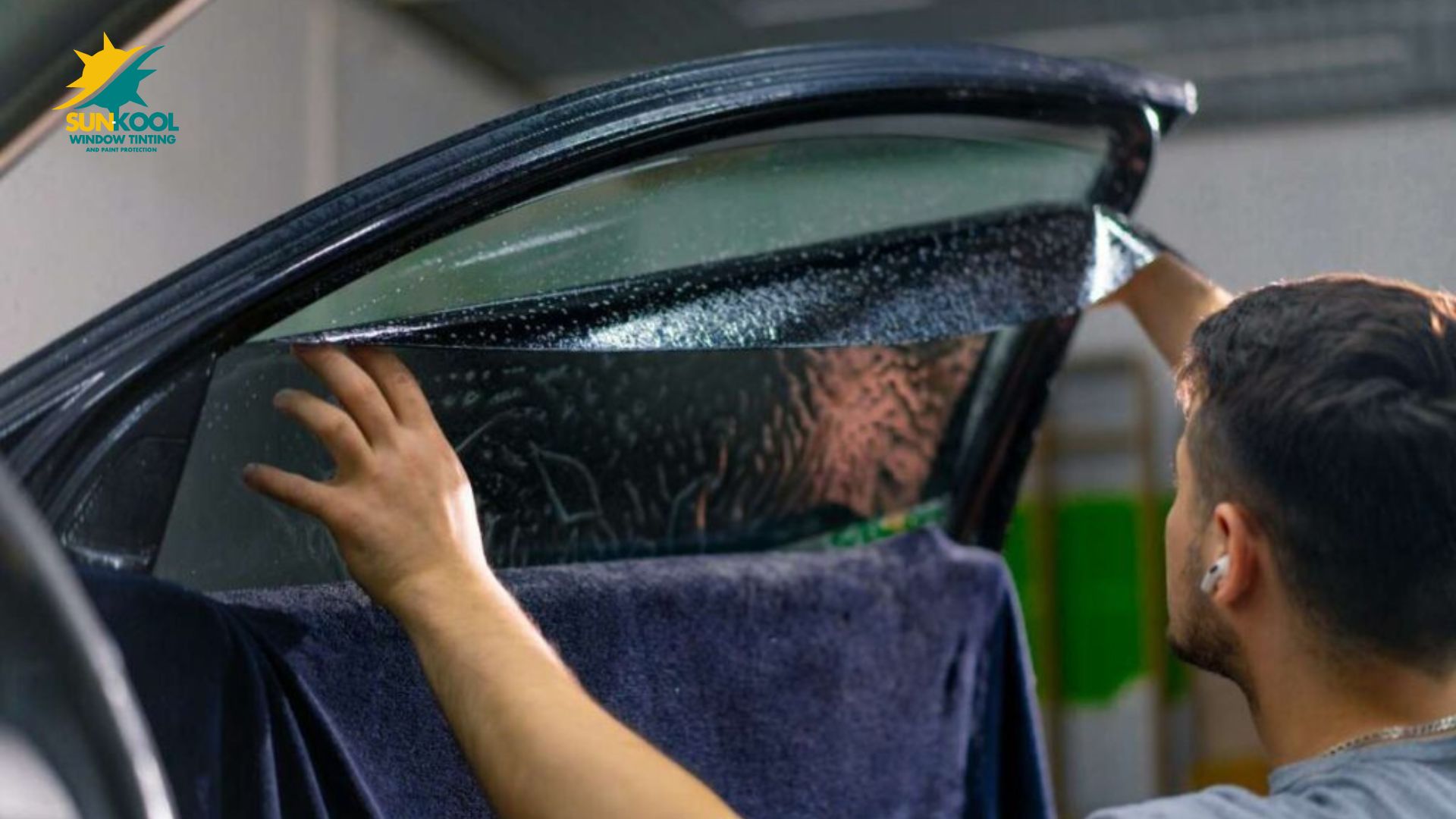 Person installing window tint film on a car door window, smoothing it down from the top while the glass remains damp.