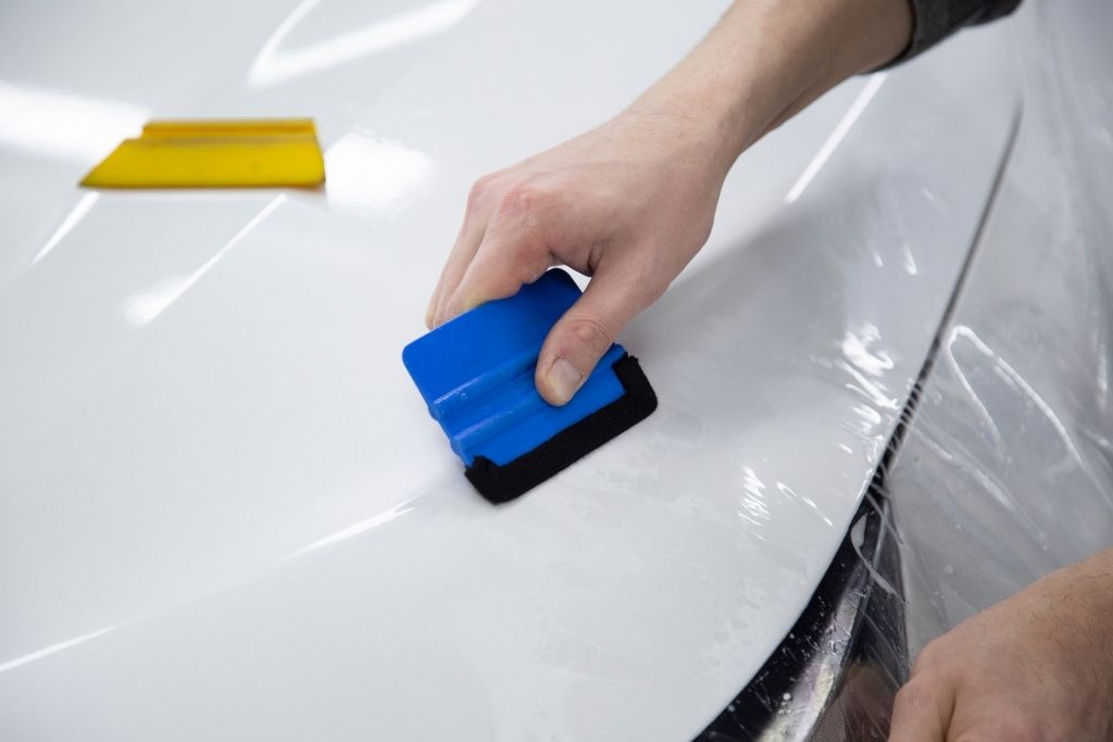 Close-up of paint protection film being applied to a white car hood with a squeegee