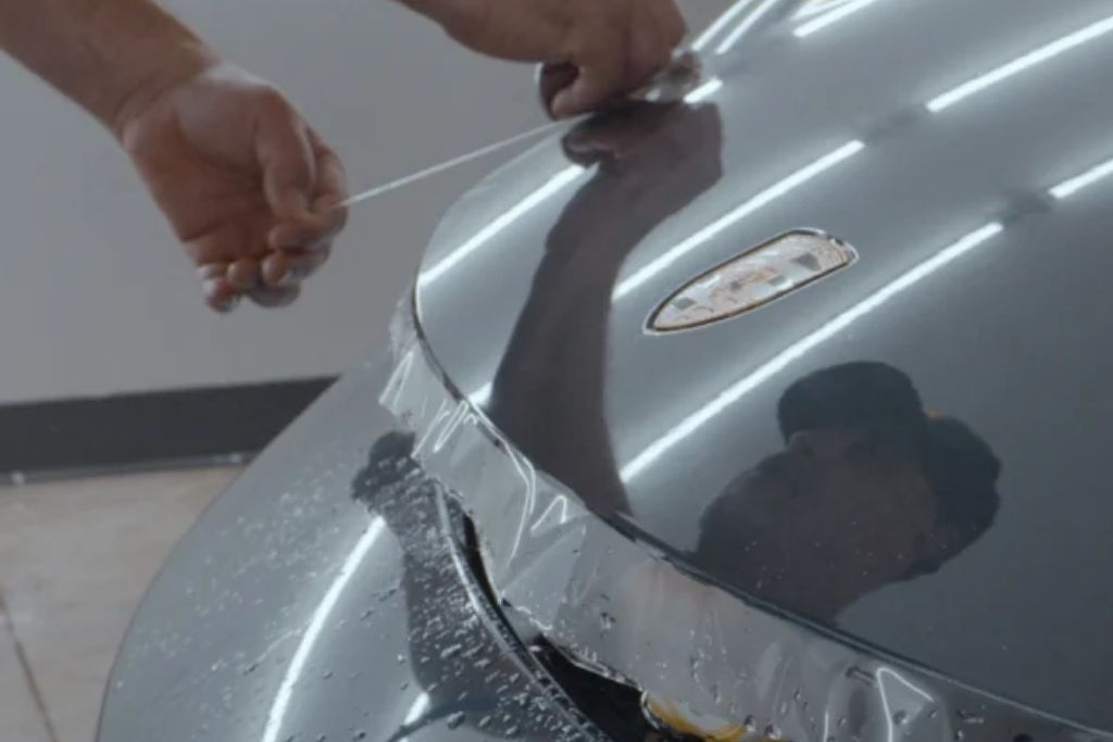 Technician applying clear paint protection film to a gray vehicle hood.